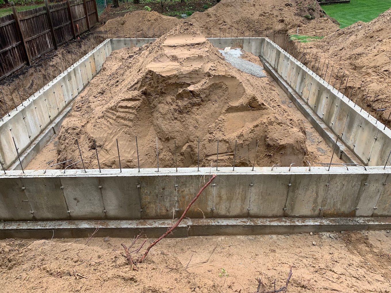 A concrete floor is being built in a backyard next to a green fence.
