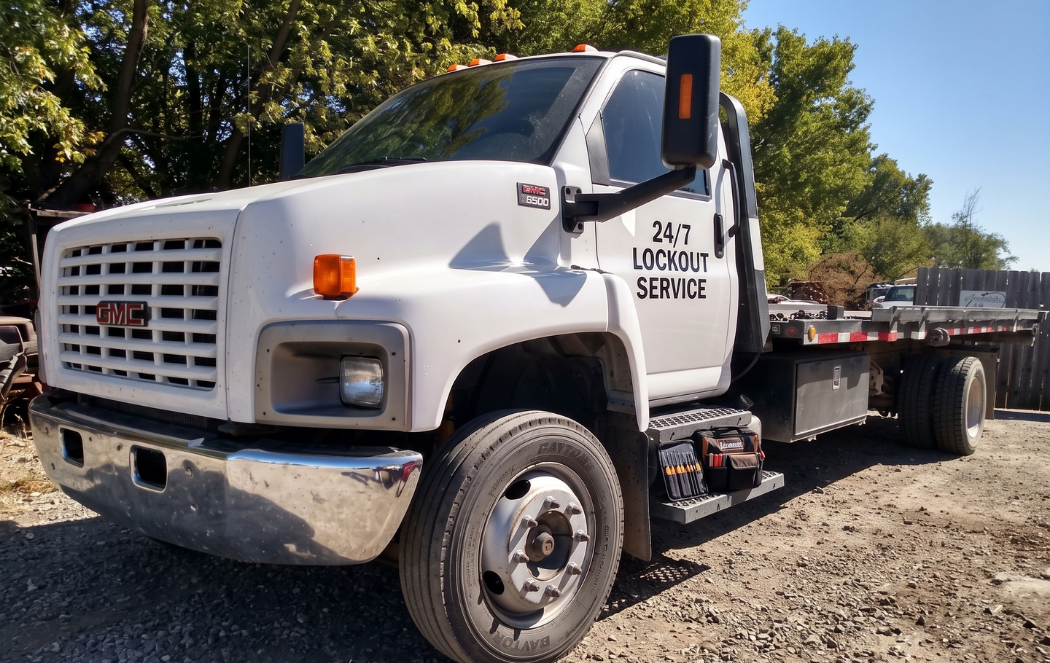 White flatbed tow truck parked on gravel with trees in the background