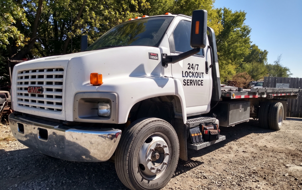 White utility tow truck parked on gravel, side view under a bright blue sky.
