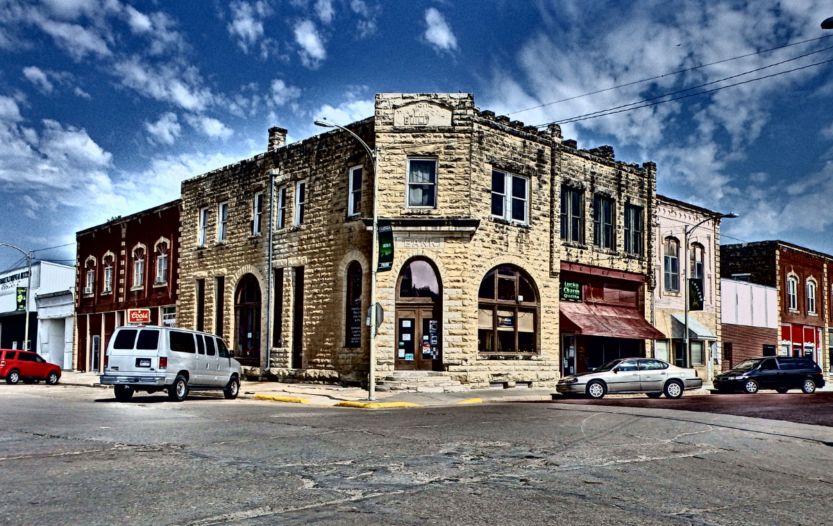 Historic stone corner building on a town street, with parked cars under a cloudy sky.