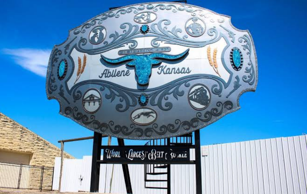 Decorative silver oval sign with blue fish motifs against a bright blue sky