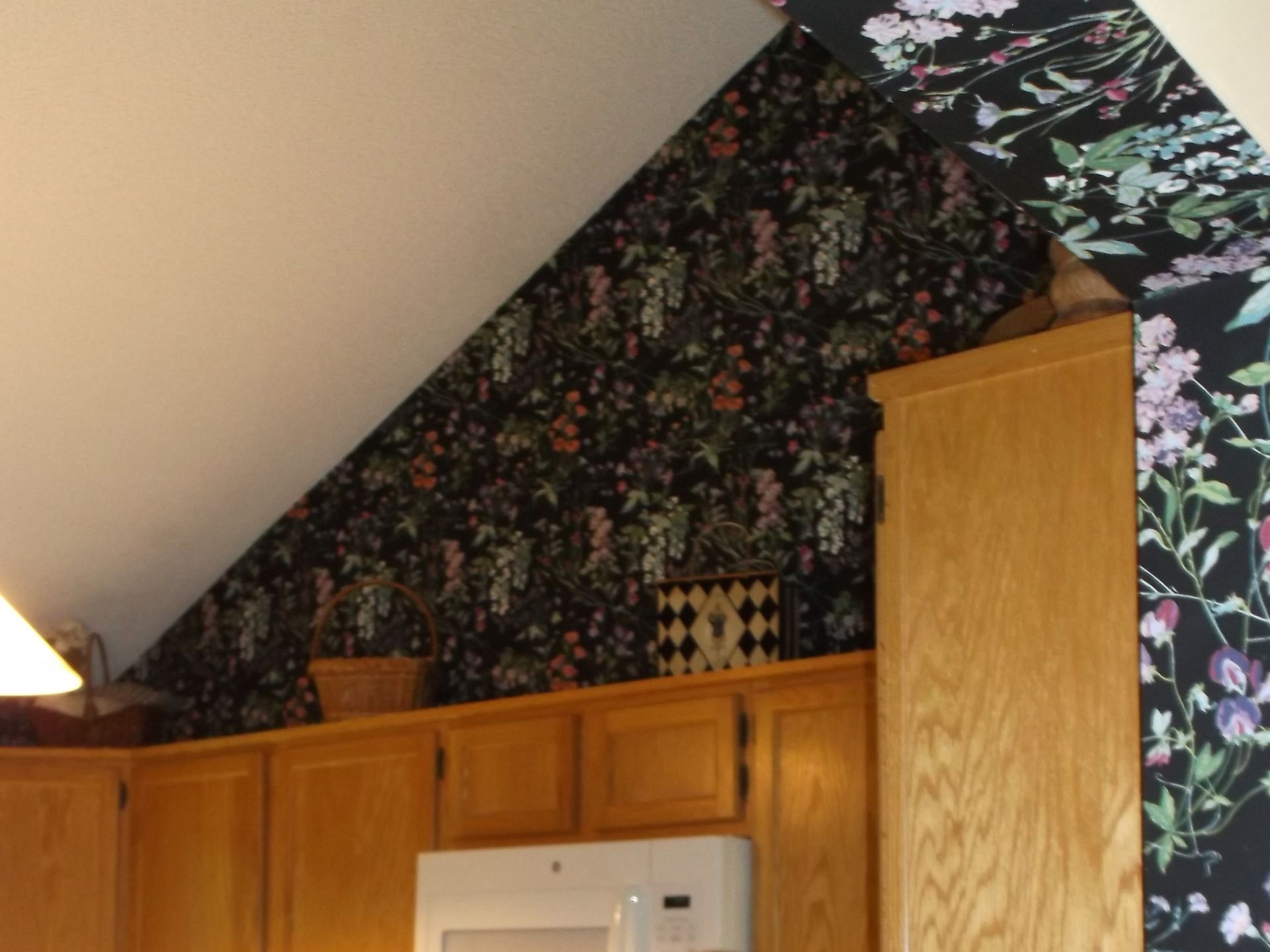 Kitchen cabinets under a sloped ceiling with dark floral wallpaper and a white stove hood