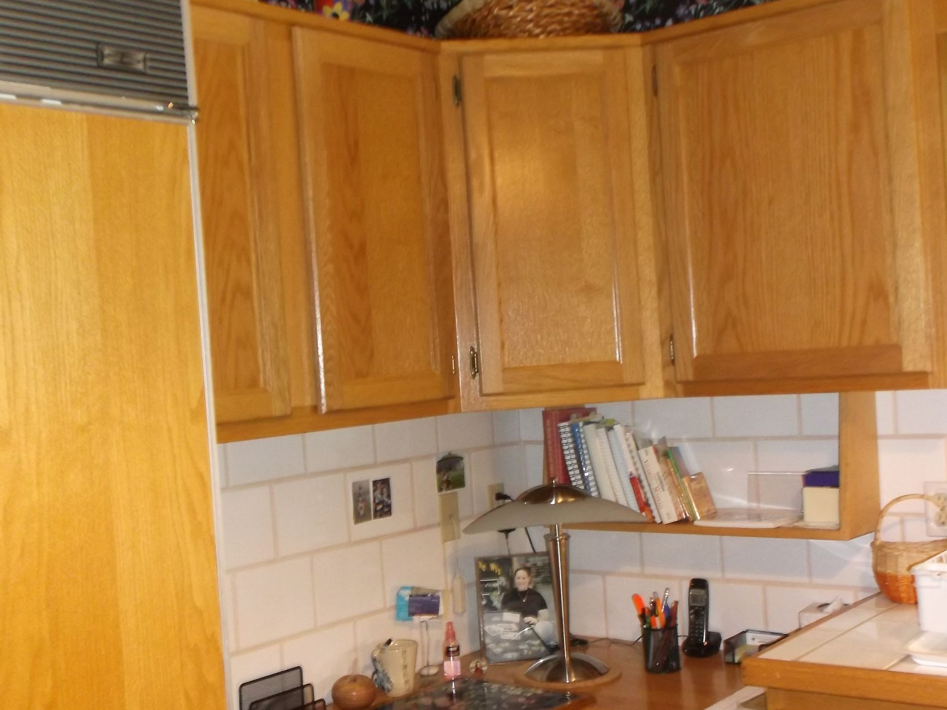 Wooden kitchen cabinets above a white tiled countertop with shelves and small items.