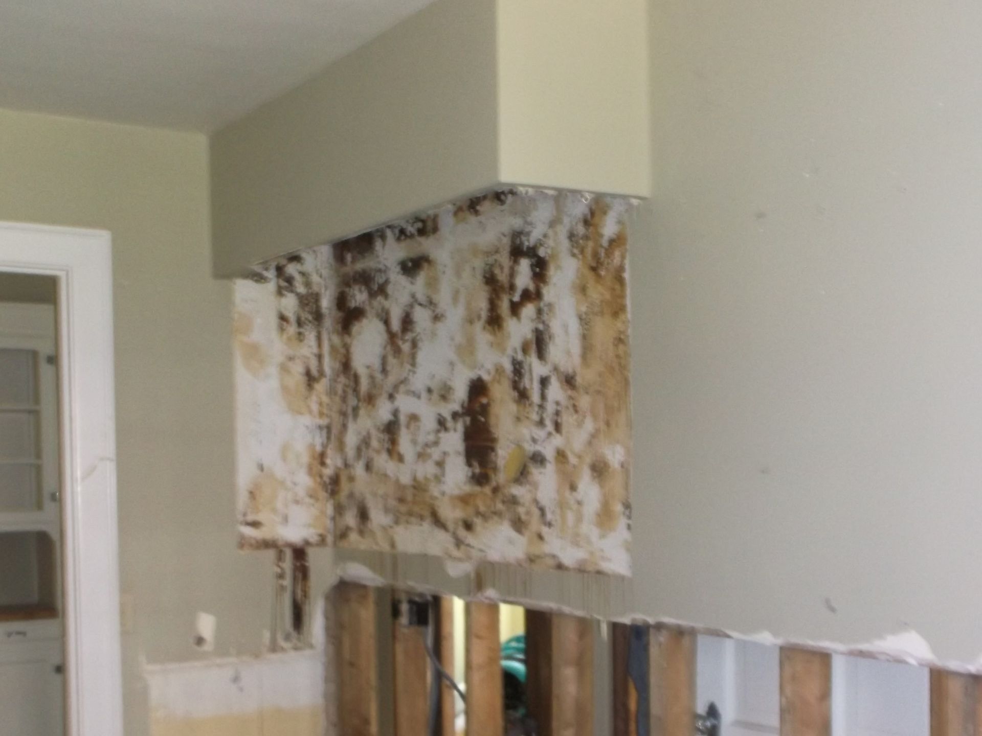 Partially removed wall cabinet with exposed studs and torn wallpaper in a room under renovation