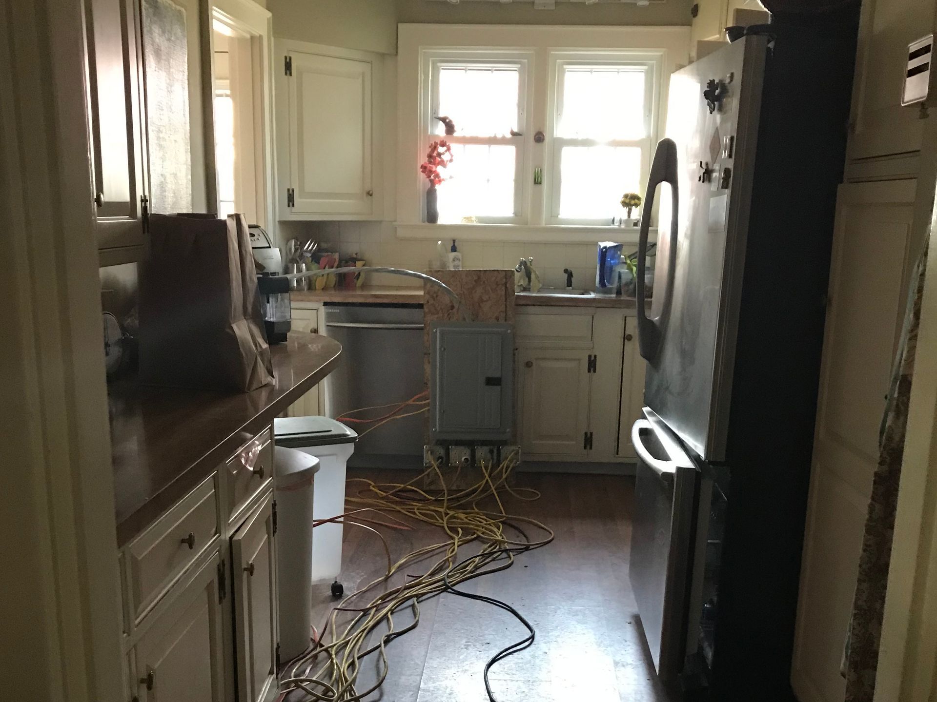 Messy kitchen with tools and cables on the floor, appliances and cabinets lining both sides.