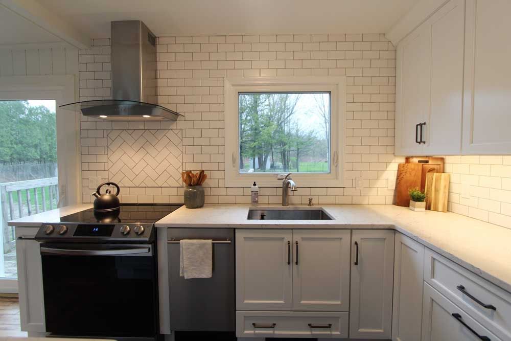 Bright modern kitchen with white subway tile, black stove, gray cabinets, and a window over the sink