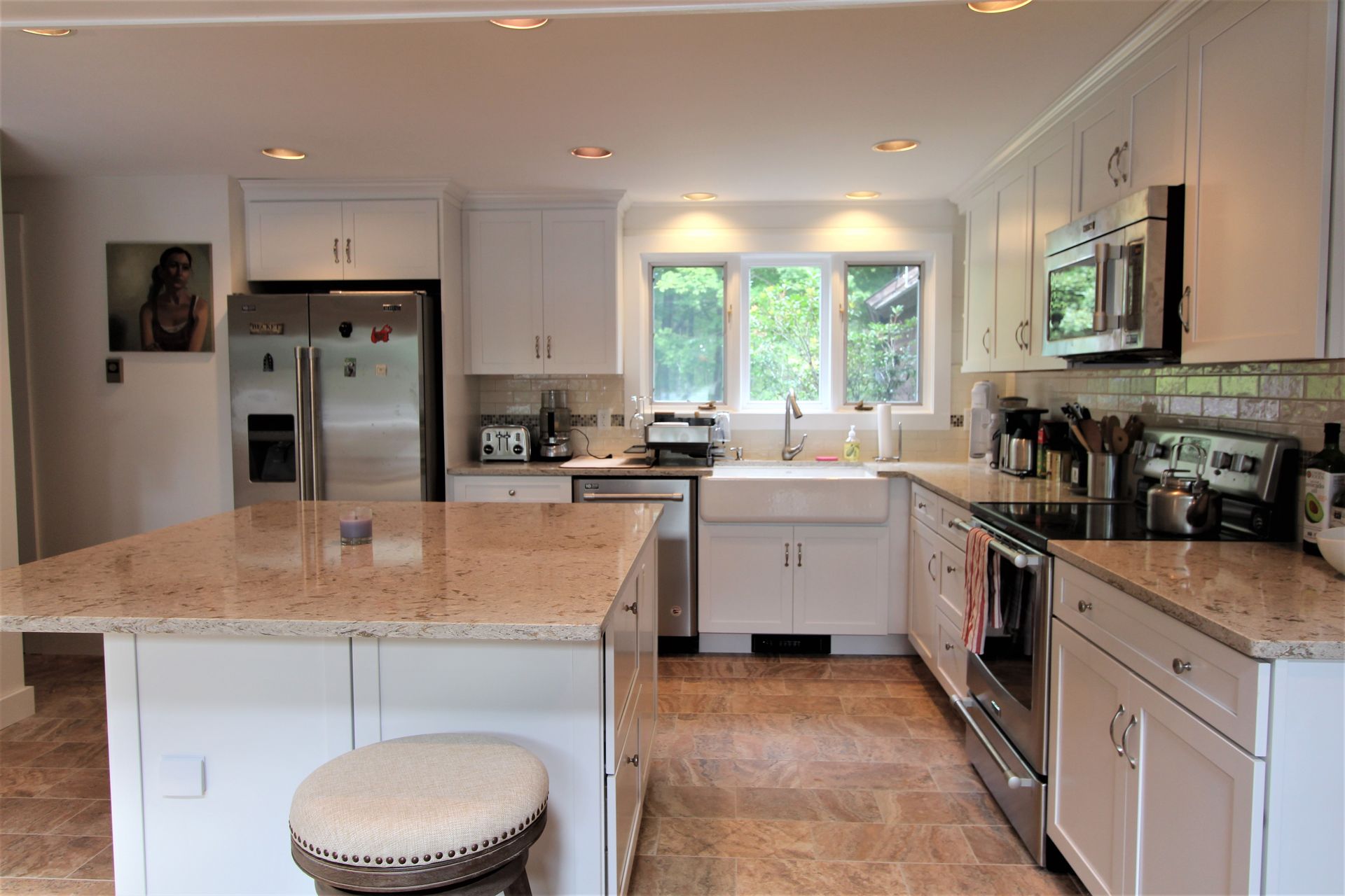 Bright kitchen with granite island, stainless appliances, white cabinets, and a window above the sink.