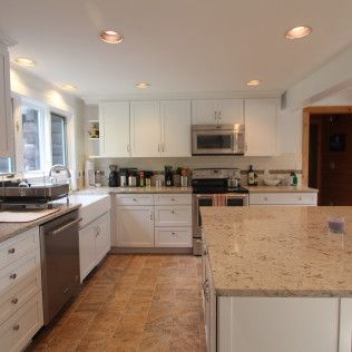 Bright white kitchen with granite island, stainless appliances, and wood-look tile floor.