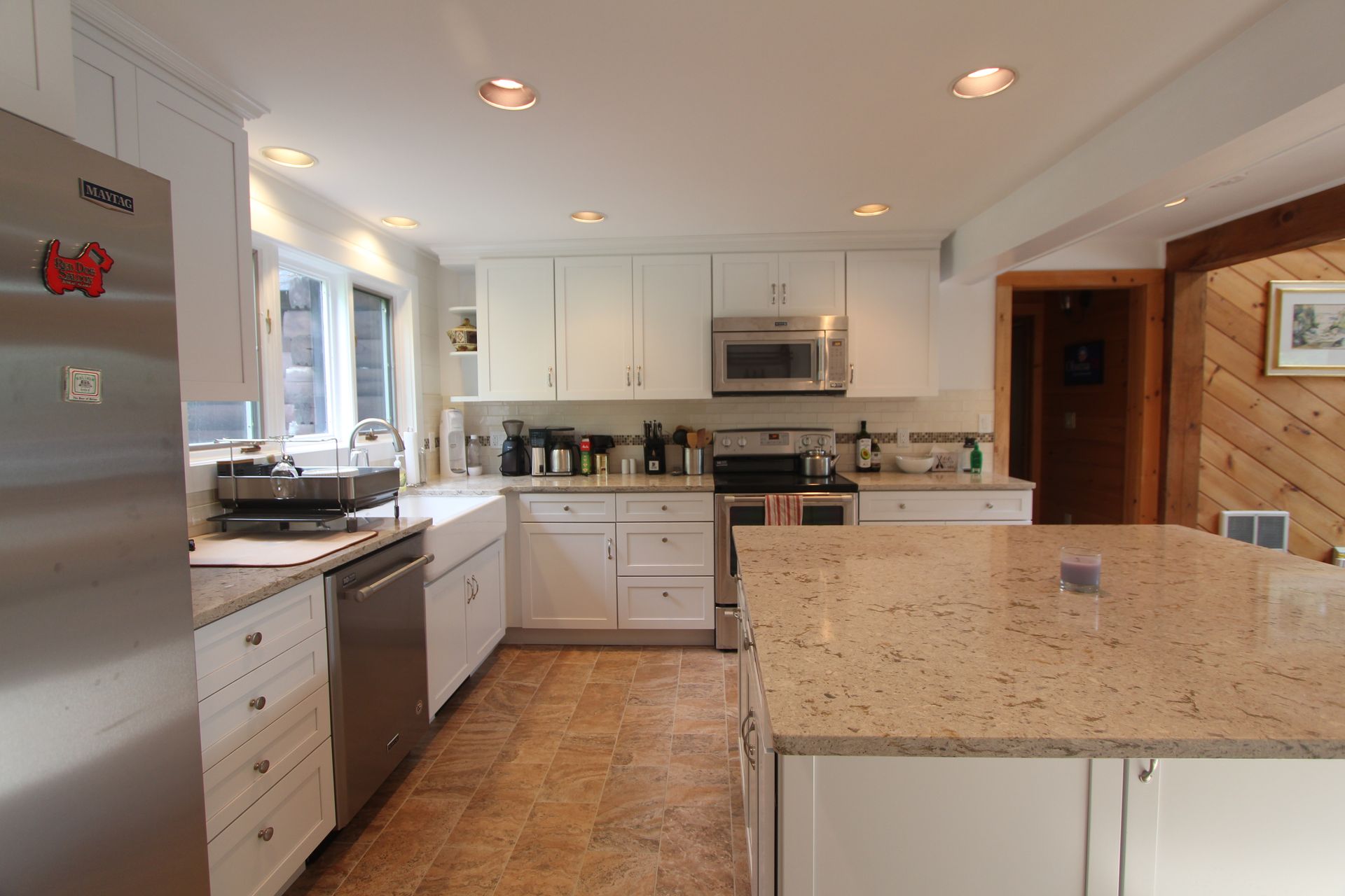 Bright kitchen with white cabinets, stainless appliances, and a granite island countertop.