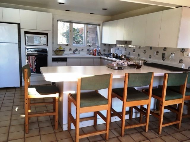 Modern kitchen with white cabinets, large island, and four wooden stools by a sunlit window