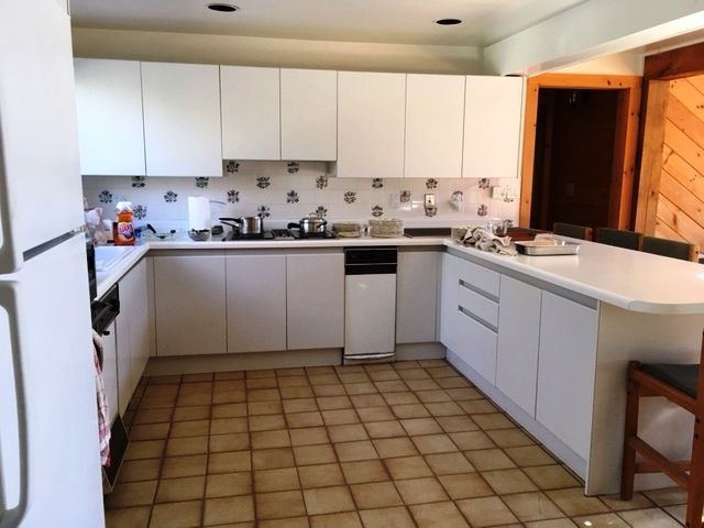 Bright kitchen with white and gray cabinets, tiled floor, countertop island, and refrigerator on the left