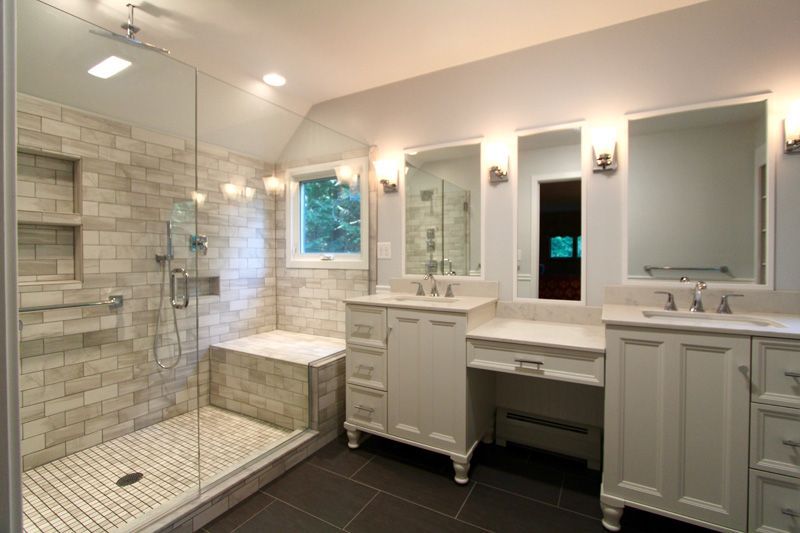 Bright modern bathroom with glass shower, white vanity, double mirrors, and black tile floor.