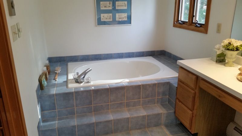 Bathroom with a tiled soaking tub, wood vanity, and window on the right