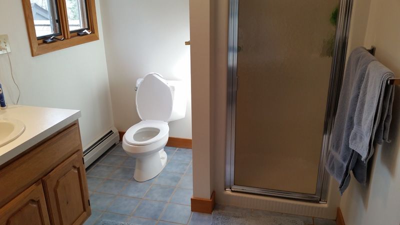 Bathroom with toilet, sink, and shower stall; towel hanging on the right wall.
