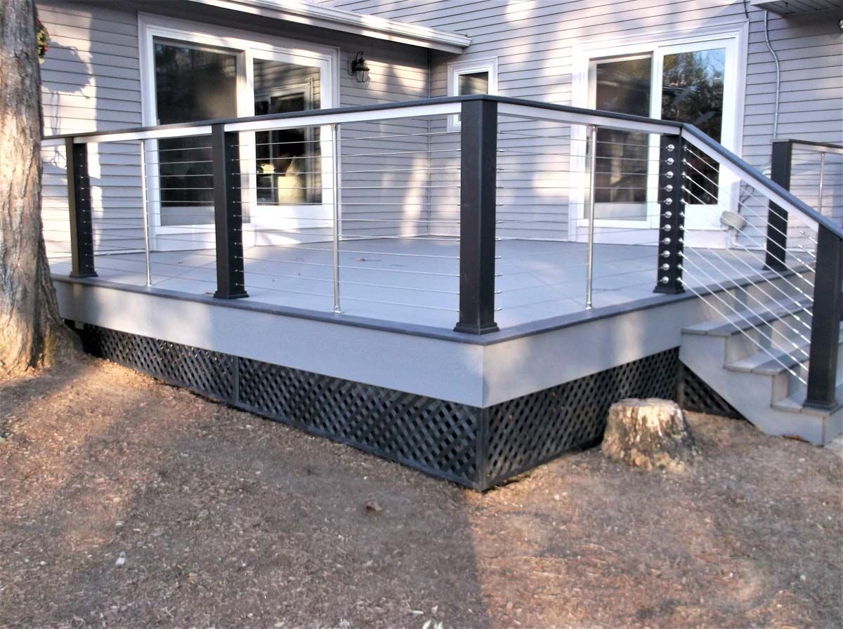 Back deck with gray railing and stairs beside a white house, viewed from a dirt yard