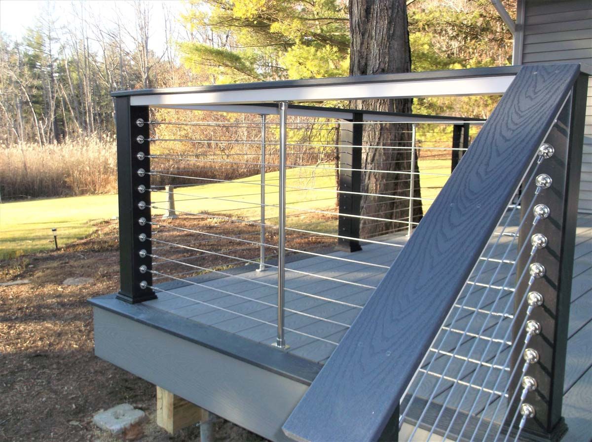 Modern outdoor deck ramp with black railings and cable sides, set in a grassy yard with trees.