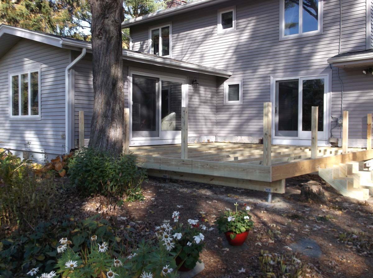 House exterior with a wooden deck, sliding glass door, and garden plants in front