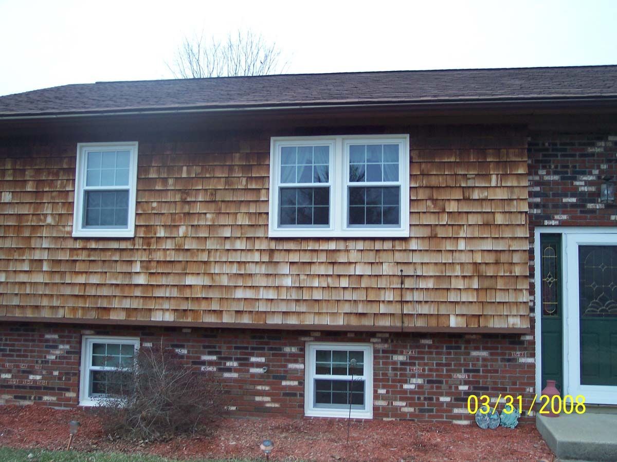 Side of a house with cedar shingles, brick base, and several windows under a dark roof.