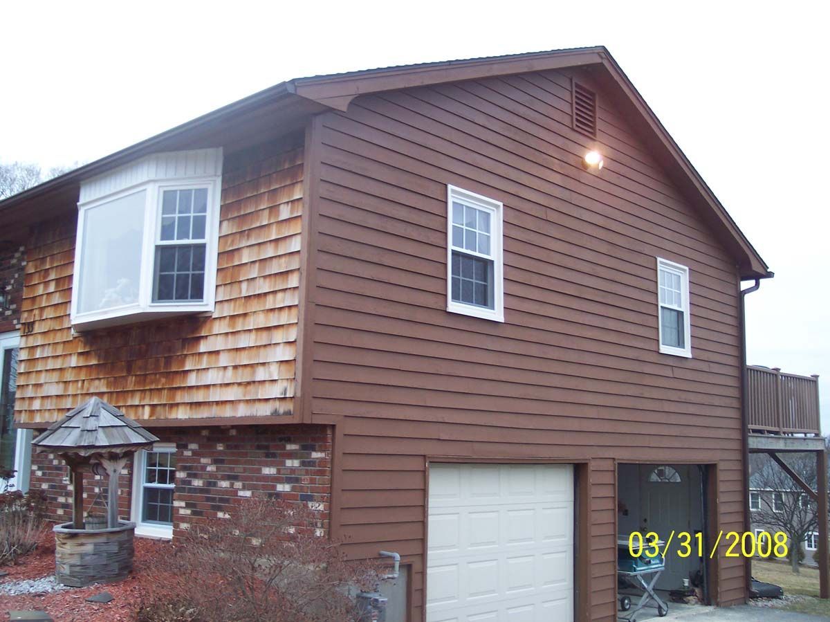 Two-story house with brown siding, white-trim windows, garage, and bay window, viewed from the front-left.