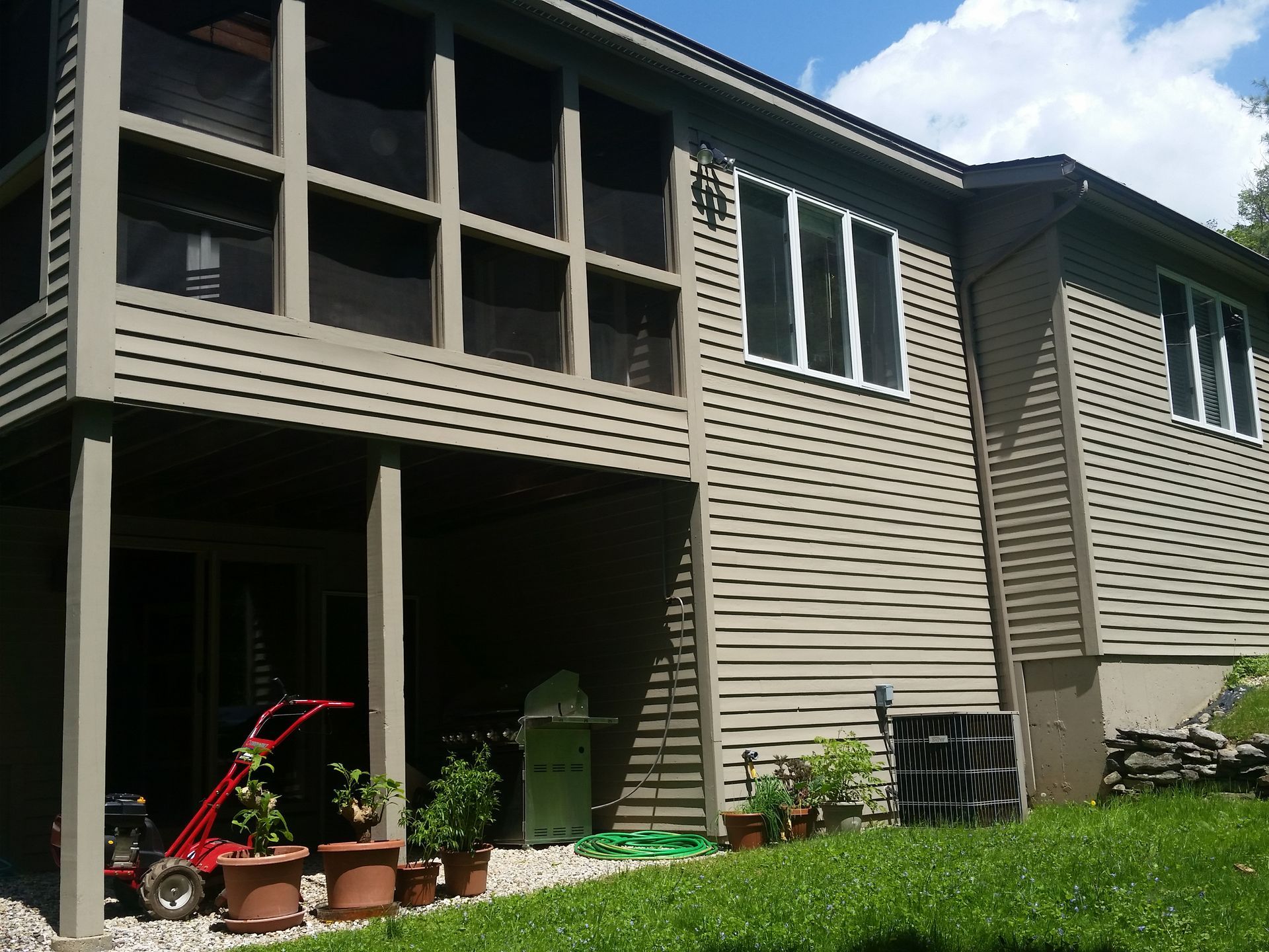 Two-story beige house with a covered patio, potted plants, and a red stroller in the yard