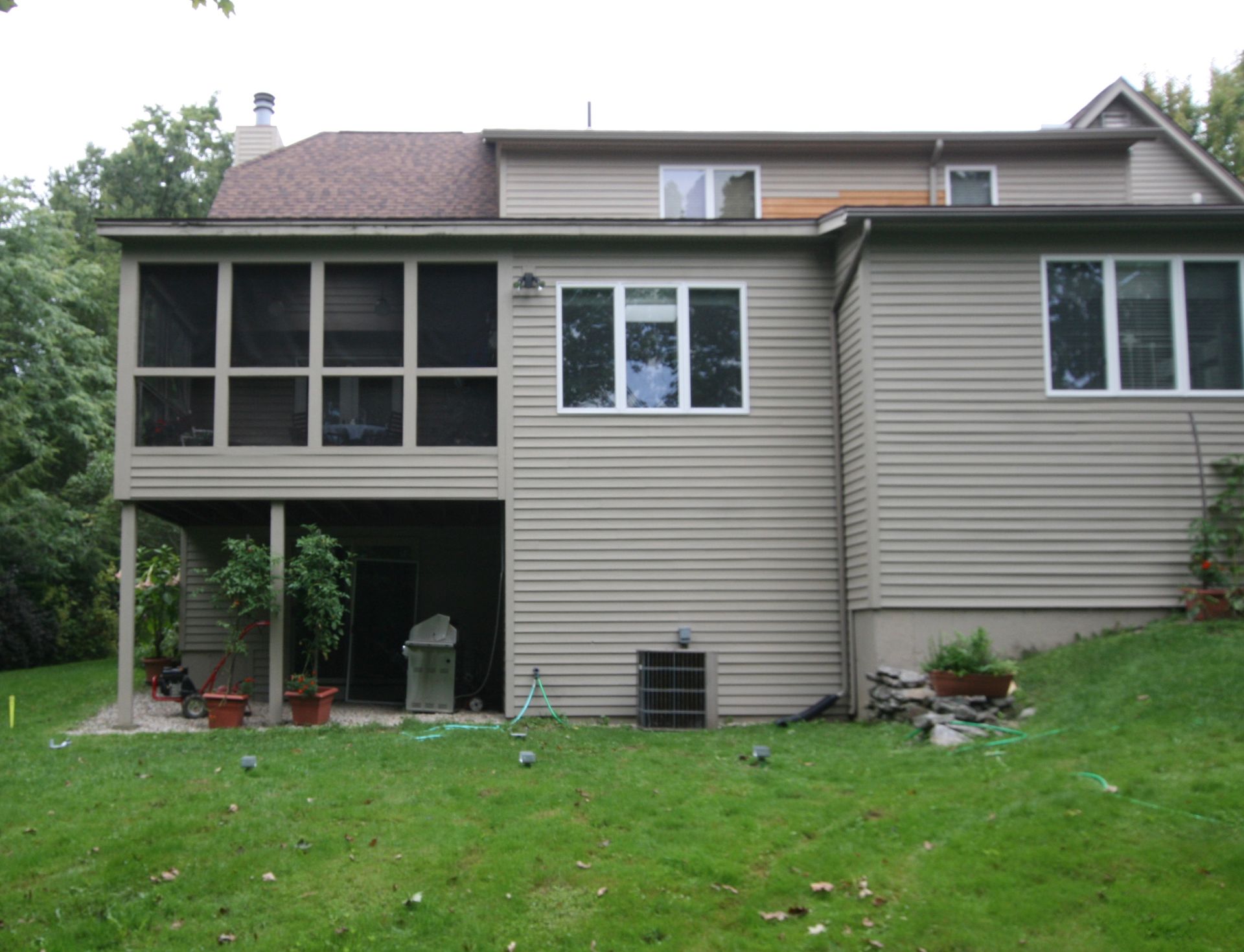 Rear view of a beige house with a screened porch and green sloped lawn