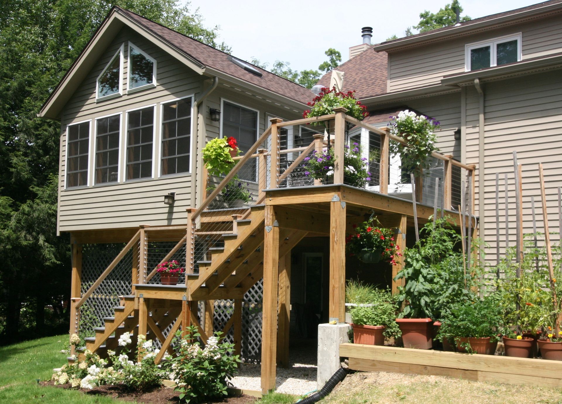 Backyard deck with stairs, potted plants, and a beige house with large windows