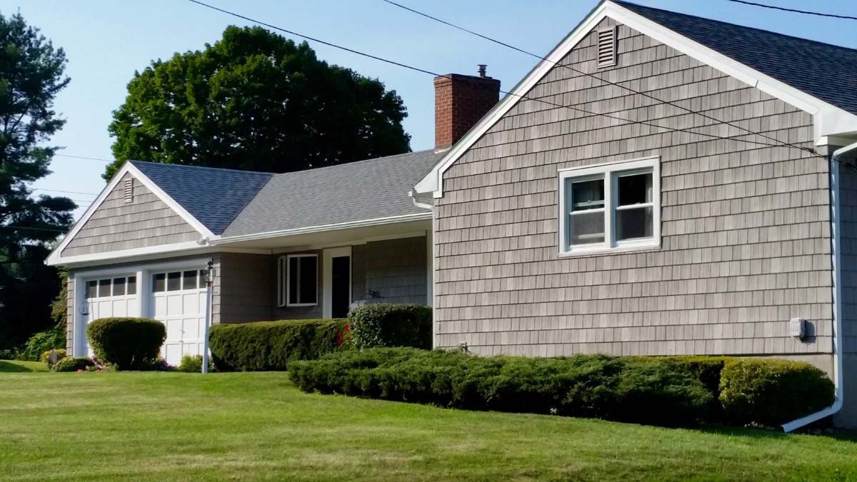 Single-story beige house with a sloped roof, white trim, and a green lawn under a clear blue sky