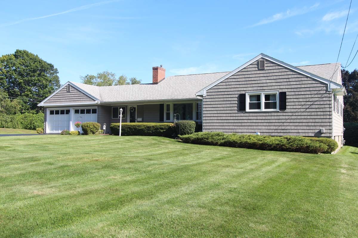 Single-story gray house with a large green lawn and a covered front porch under a blue sky