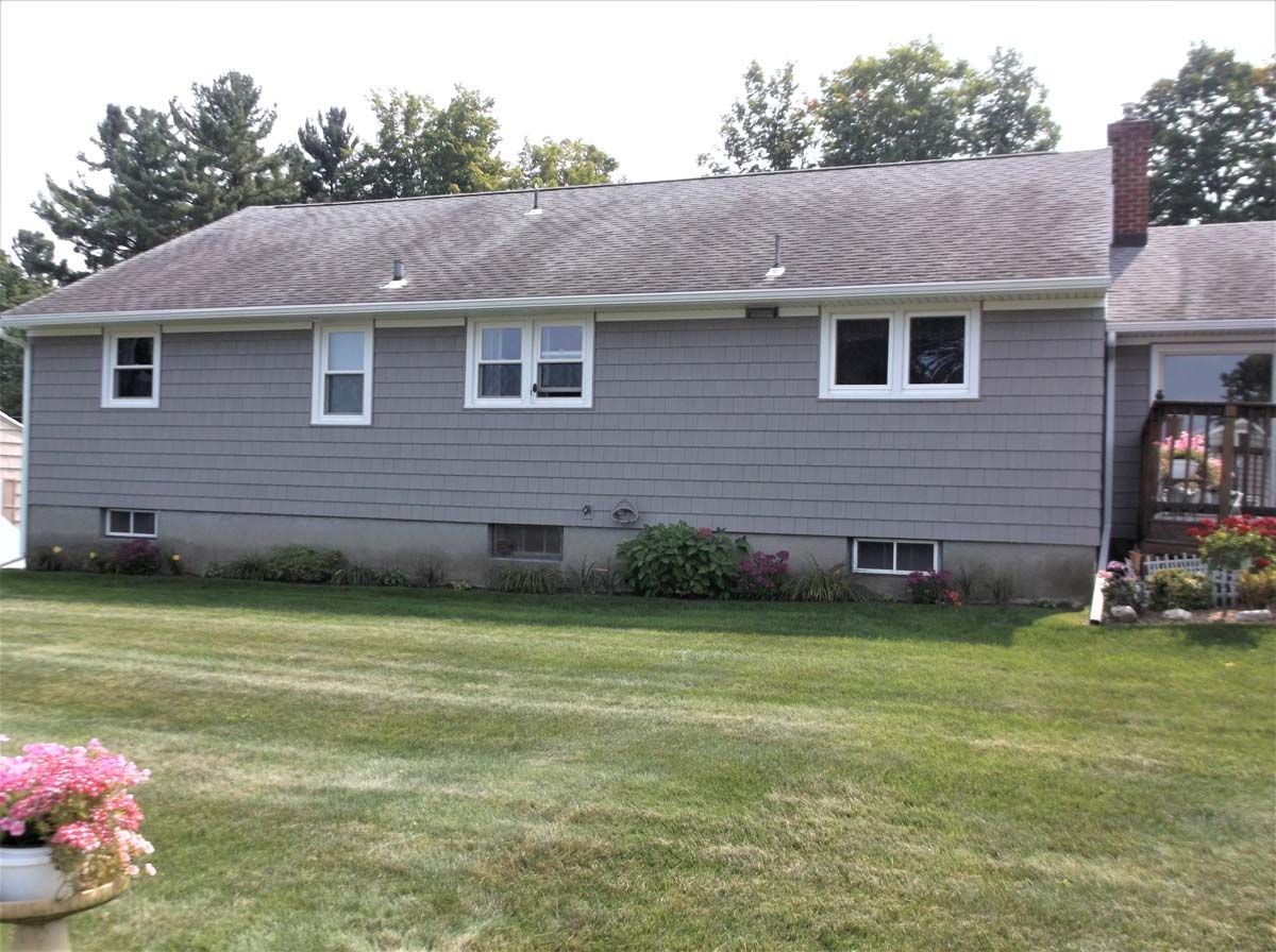 Gray single-story house with a front lawn and small flower bed under trees