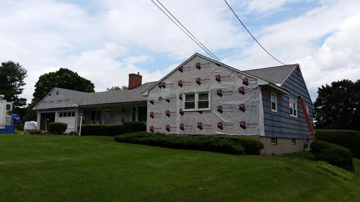 Two-story house with blue siding and a white patterned exterior, set on a green lawn under a cloudy sky