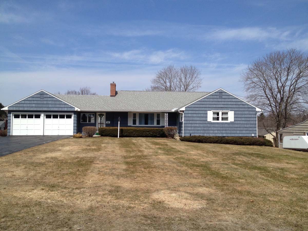 Single-story blue house with a two-car garage and a patchy front lawn under a clear sky