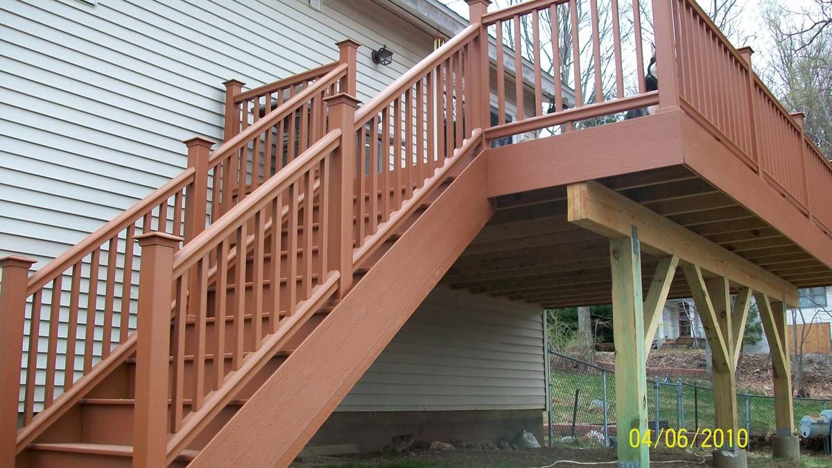 Wooden deck staircase with railings attached to a house, raised over a sloped yard.