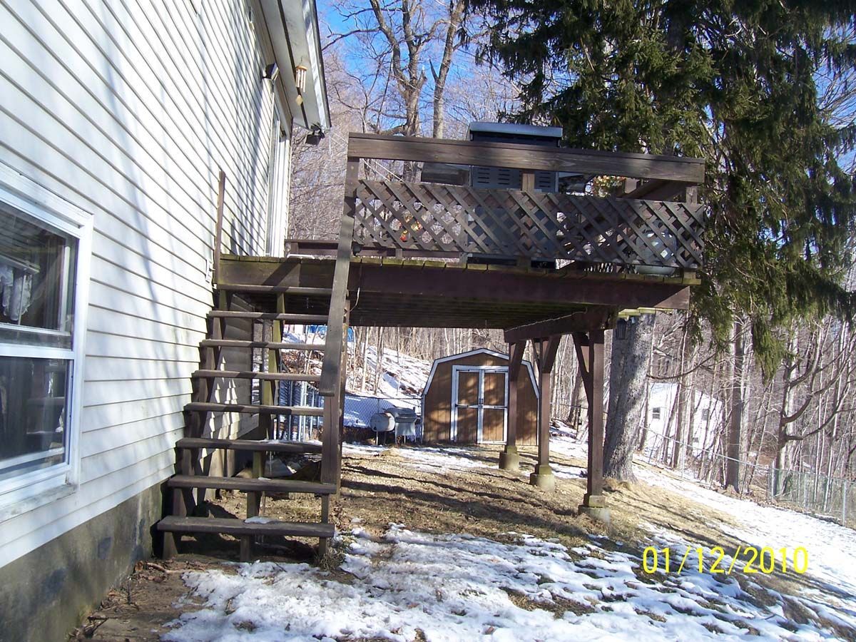 Wooden stairs and deck attached to a house in a snowy yard with trees in the background
