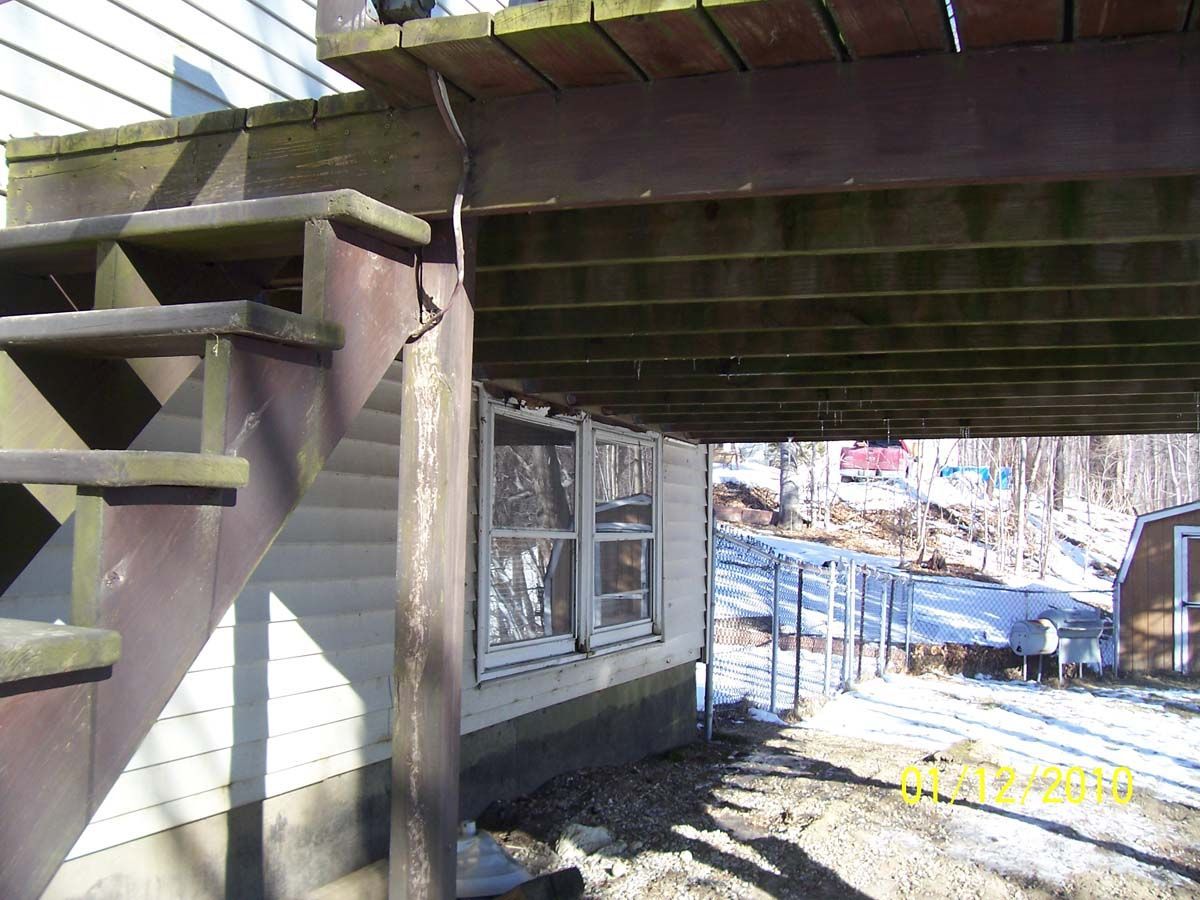 Under an outdoor deck, a basement window with snow-covered ground and wooden supports overhead
