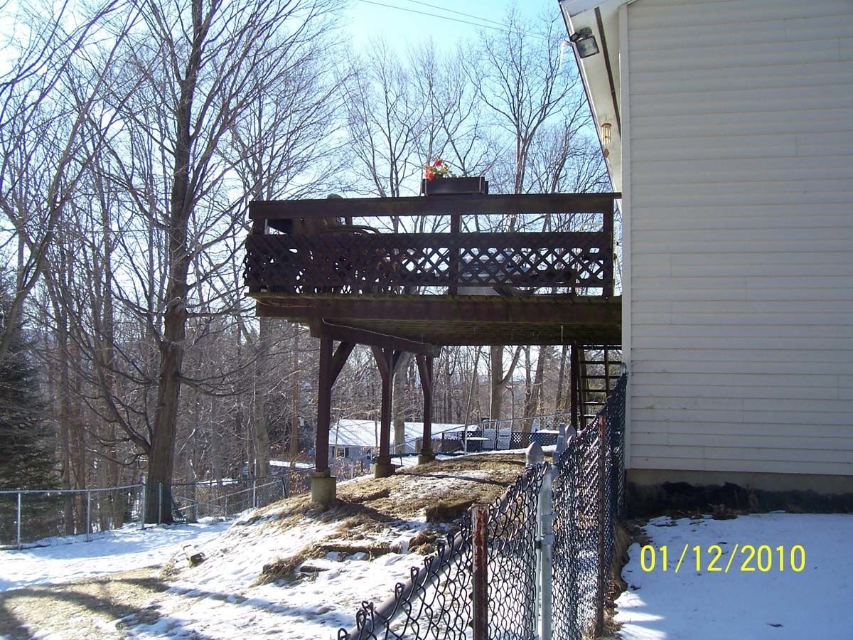 Snowy backyard with a raised wooden deck beside a white house and chain-link fence.