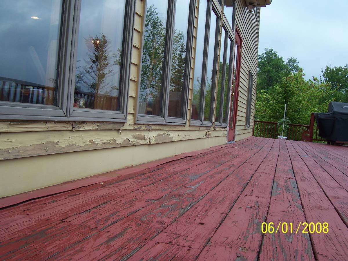 Red wooden deck beside a house with windows, leading toward a backyard and trees.