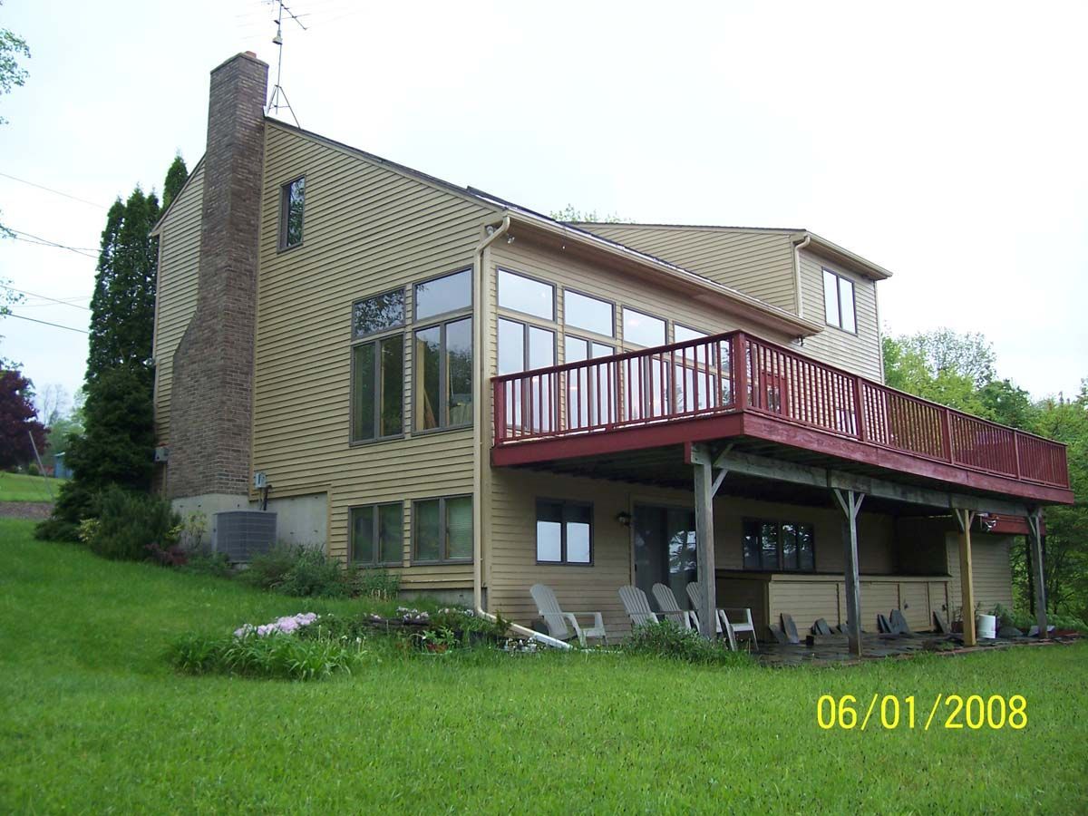 Brick house with large windows and a red deck on a grassy hillside