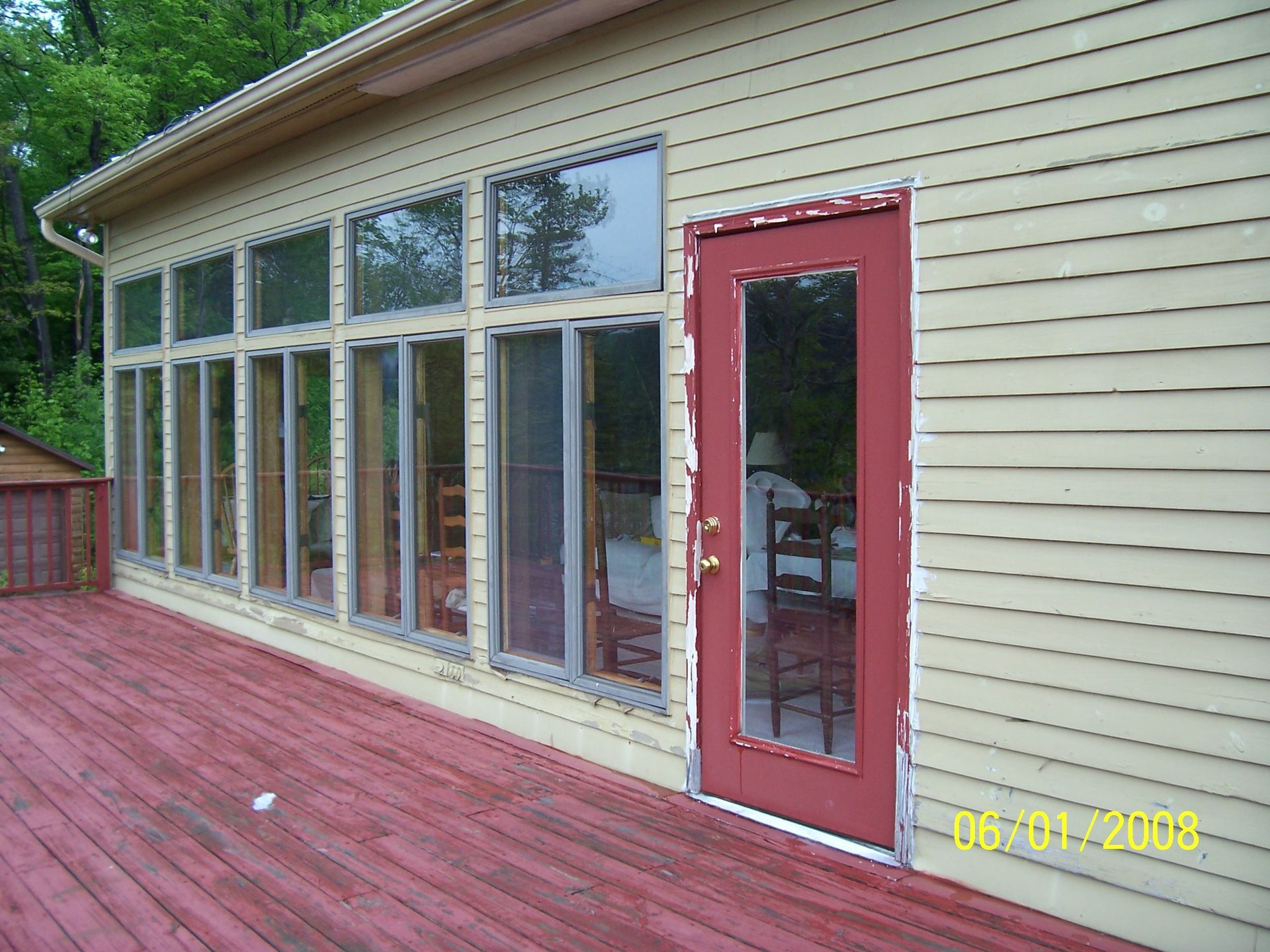 Back deck with red door, large windows, and red wooden floor on a beige house exterior
