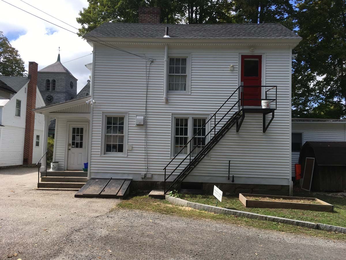 White two-story house with exterior stairs, red door, and gravel yard
