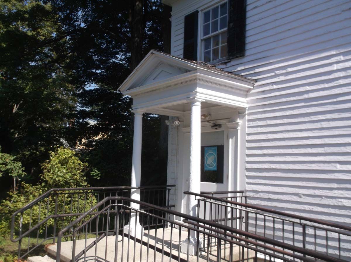 White building entrance with columns, ramp, and black railings in daylight