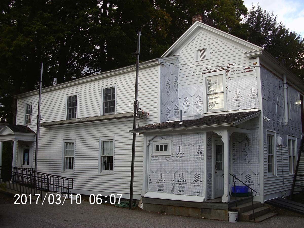 White historic house with decorative trim and porch, shown in daylight with trees behind it