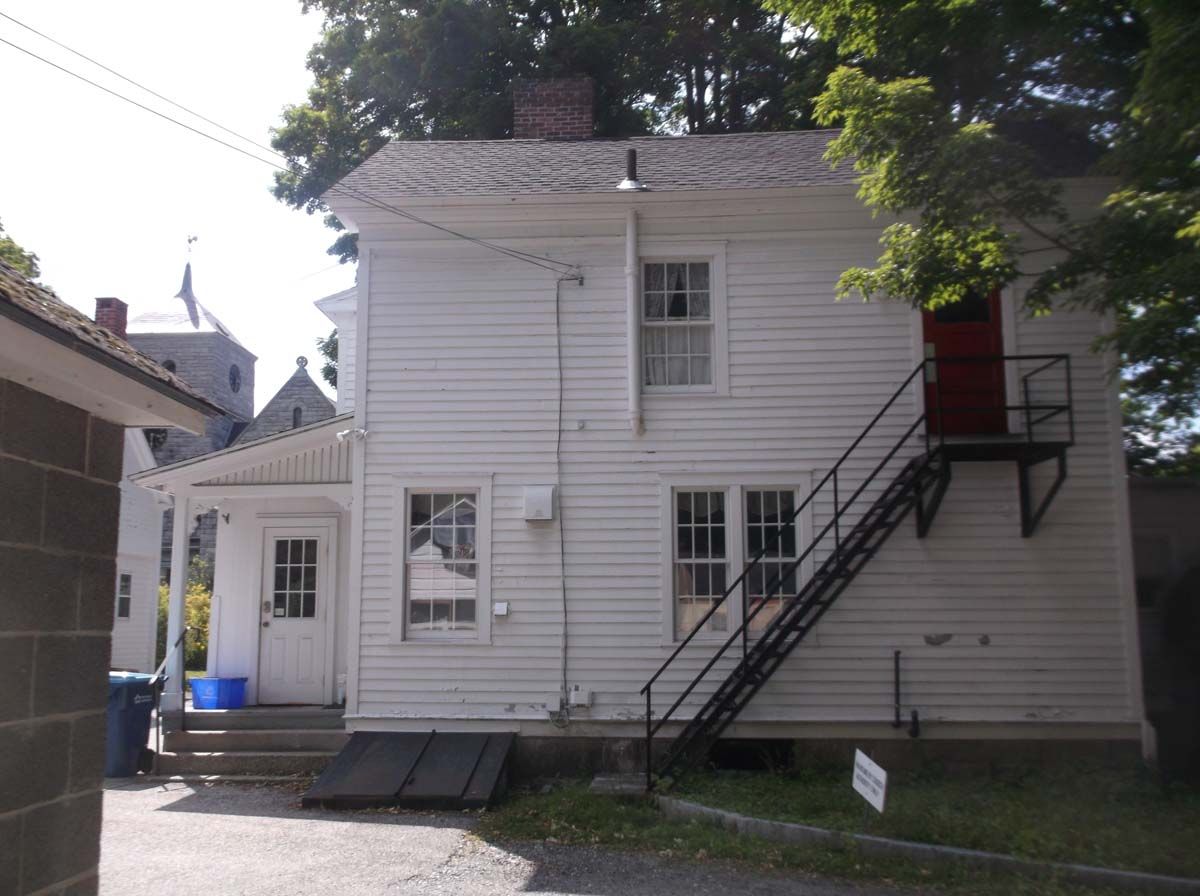 Two-story white house with black exterior stairs and a small side porch under trees.