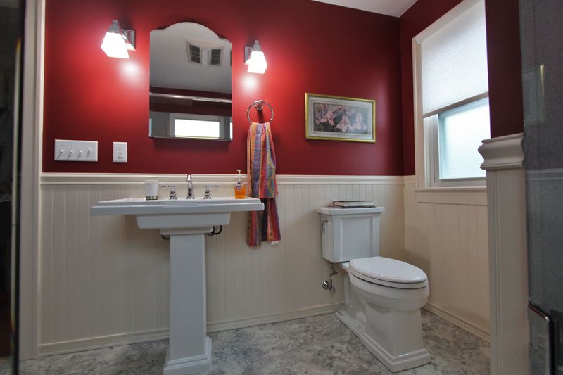 Accessible bathroom with red walls, pedestal sink, toilet, mirror, and window.
