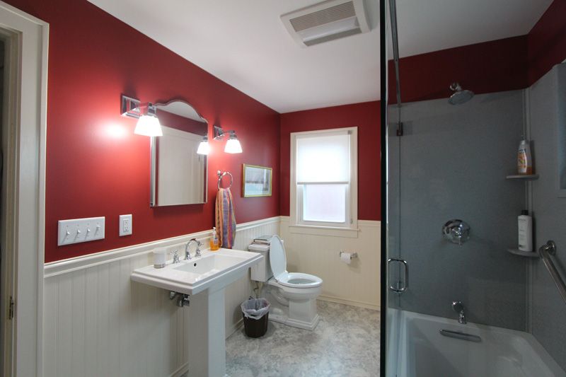 Modern bathroom with red accent wall, vanity sink, toilet, and mirrored shower enclosure
