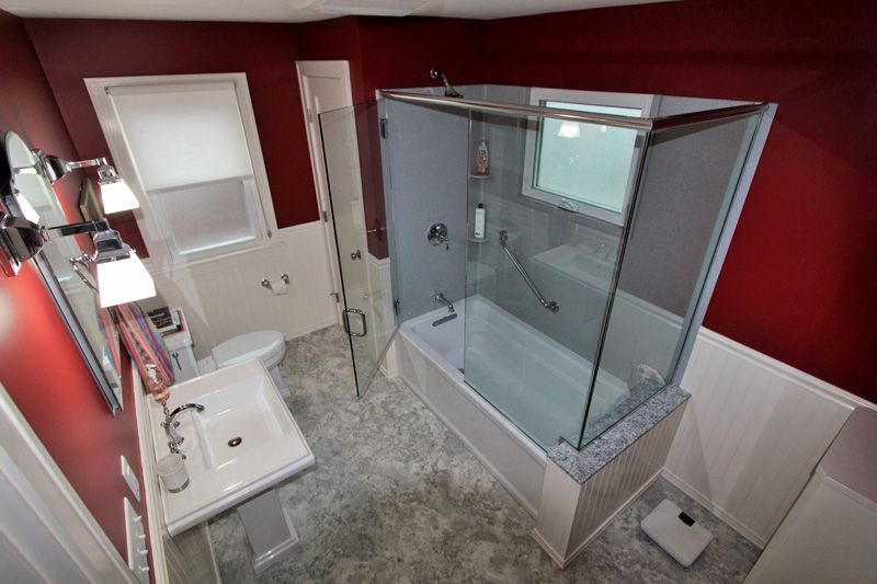 Small bathroom with white sink and toilet, red walls, and a glass-enclosed shower.