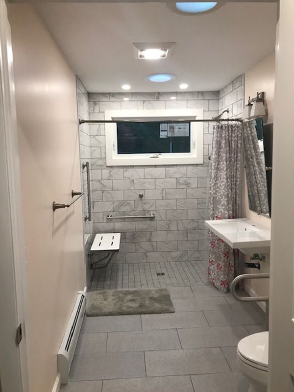 Narrow bathroom with tiled floor, shower area, sink, toilet, and frosted window.