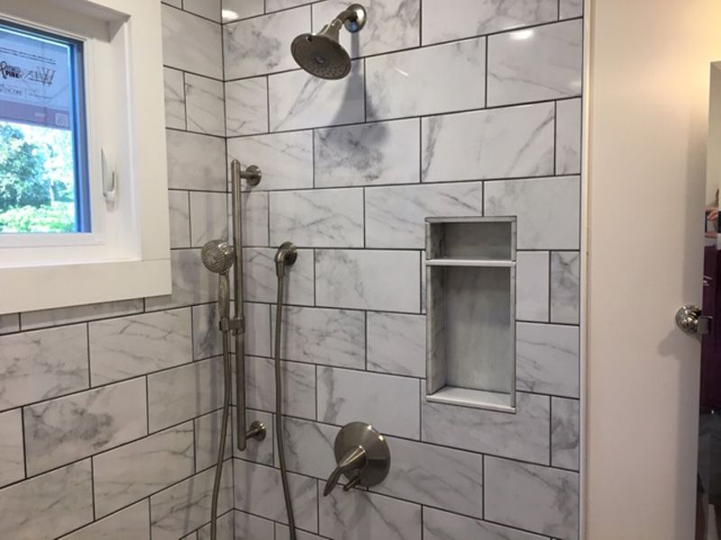 Tiled shower with chrome fixtures, window, and recessed niche in a bathroom