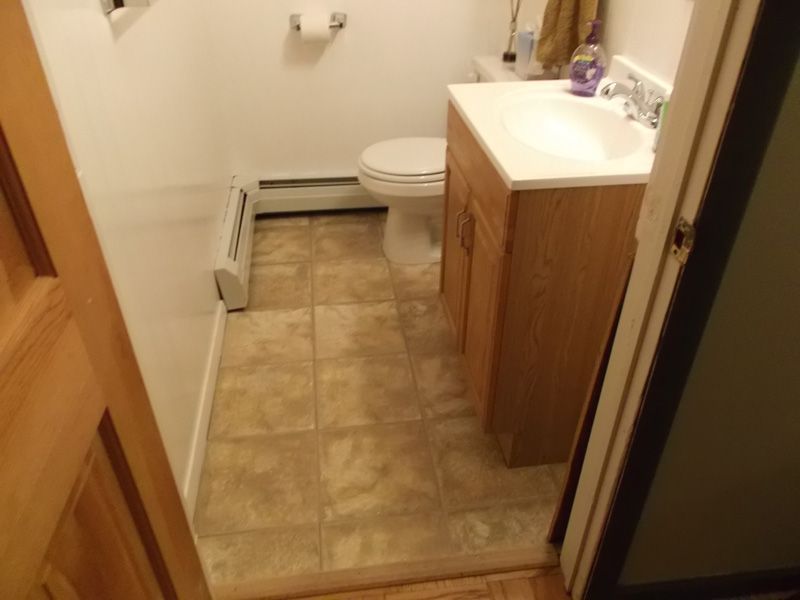 Small bathroom with beige tile floor, wooden vanity, sink, and toilet, viewed through an open door