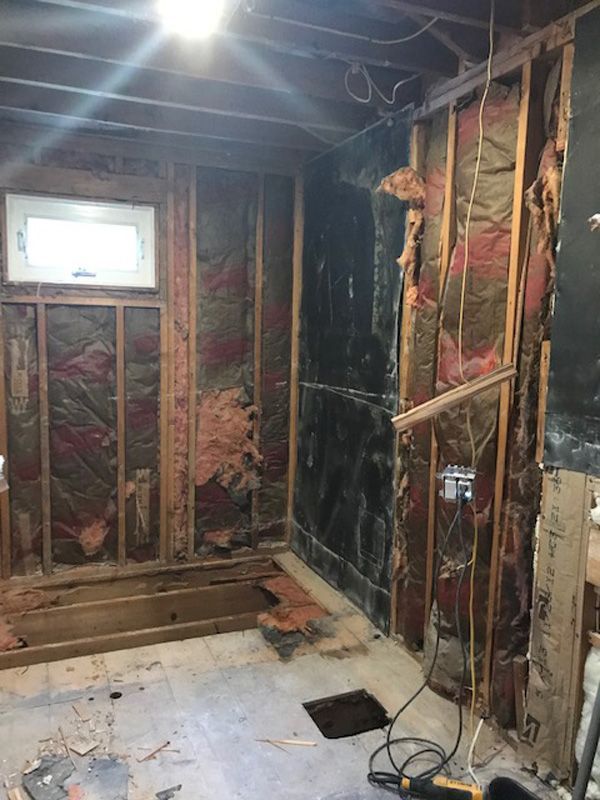 Partially demolished room with exposed studs, insulation, and a single bright work light overhead