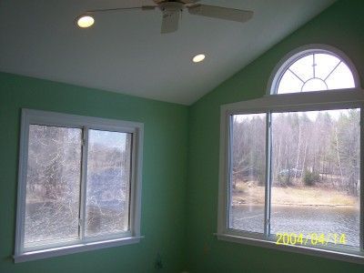 Green room with two windows, a vaulted ceiling, and a large arched window overlooking trees and water